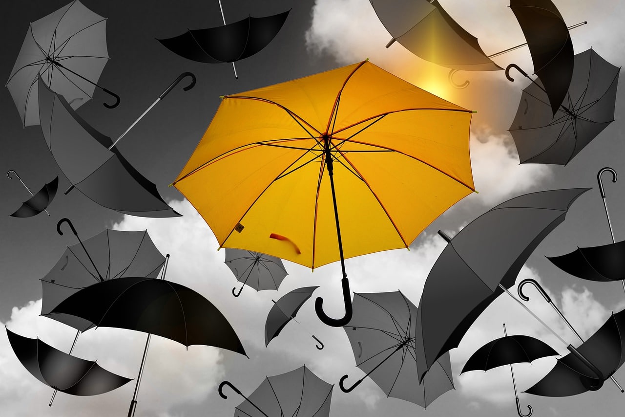 A yellow umbrella mixed with grey and black umbrellas