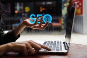 A woman's hand holding the word SEO sat at a laptop