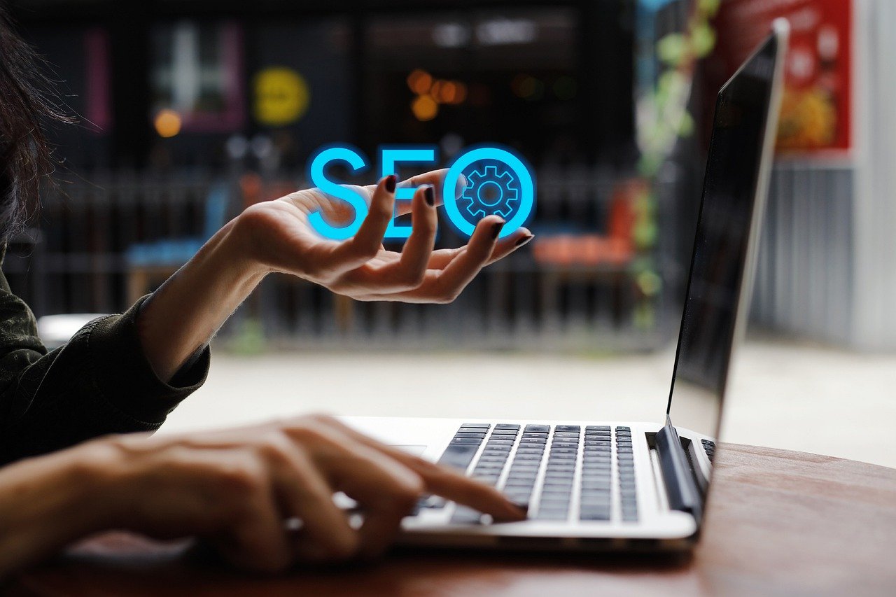 A woman's hand holding the word SEO sat at a laptop